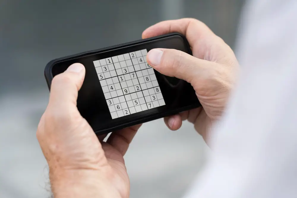 This photo depicts a man playing a Sudoku game on his smartphone.
